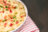 A bowl of mashed potatoes topped with bacon bits and chives, on a striped cloth.