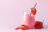 A glass of strawberry smoothie with a red and white polka dot straw, garnished with strawberry halves.