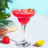 A strawberry margarita in a margarita glass, garnished with a strawberry slice, with a wooden juicer and lime wedge on the side.